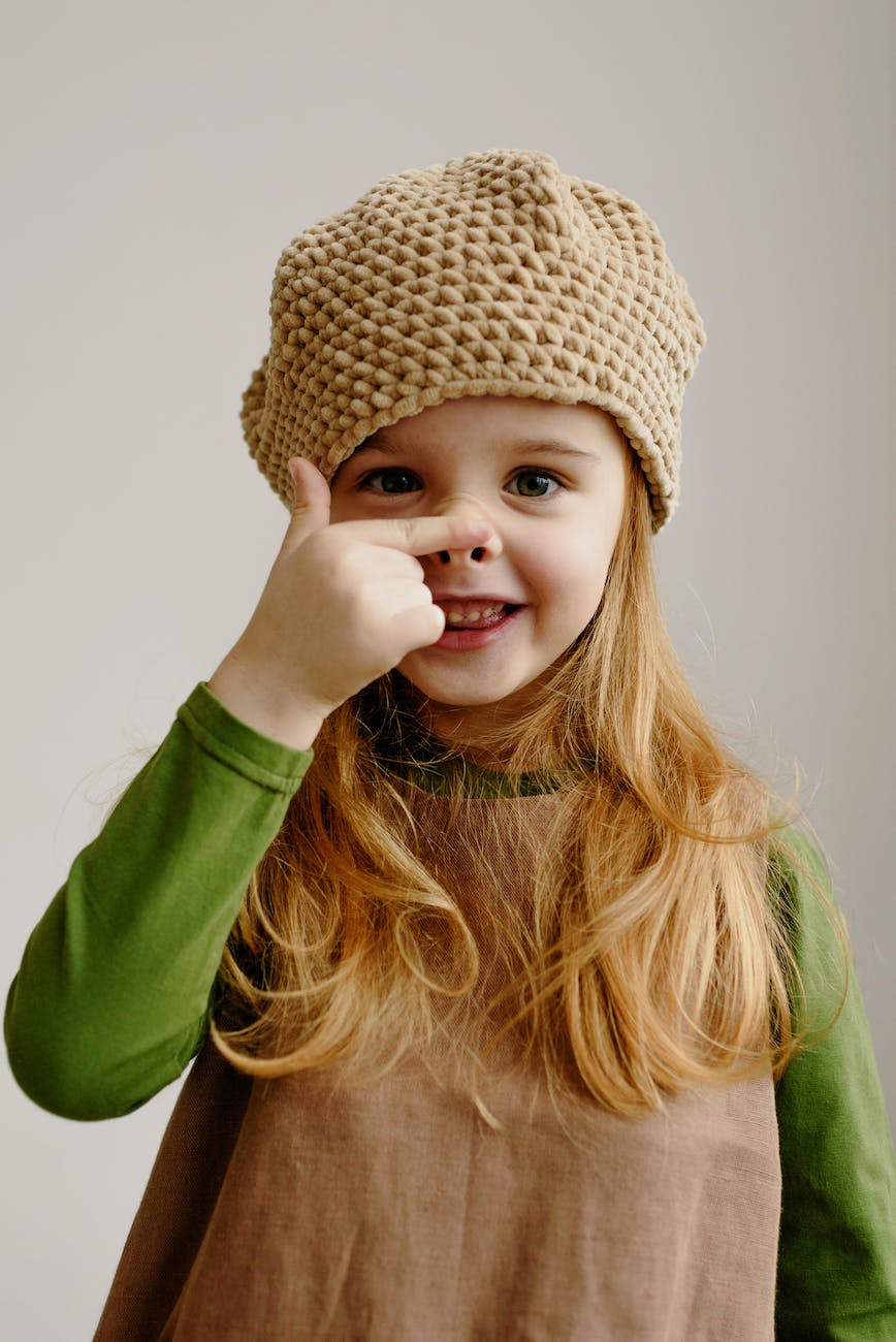 girl in green long sleeved shirt with beige beanie pressing her nose